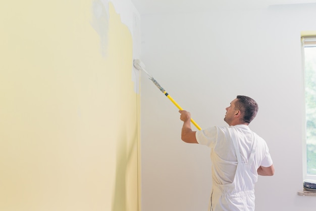 労働者の男はアパートの壁にペンキとパテを塗り、新しい家で修理をします