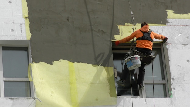 Worker man insulates wall high-rise building