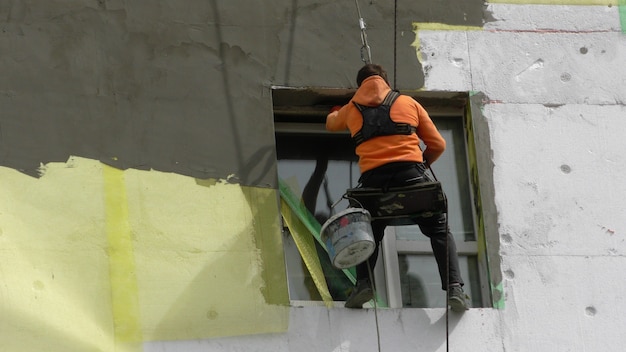 Photo worker man insulates wall high-rise building