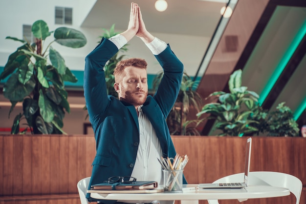 Worker man in suit meditating at desk in office.