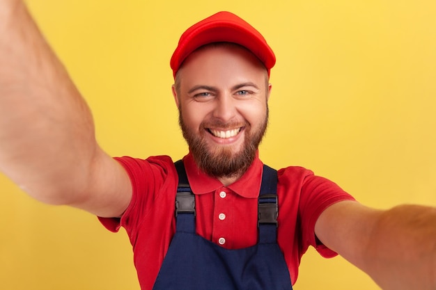 Foto uomo lavoratore con uniforme blu che indossa un selfie guardando la fotocamera con un sorriso a trentadue denti pov