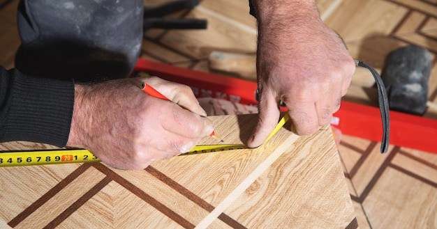 Worker marking ceramic tile with pencil and measuring tape