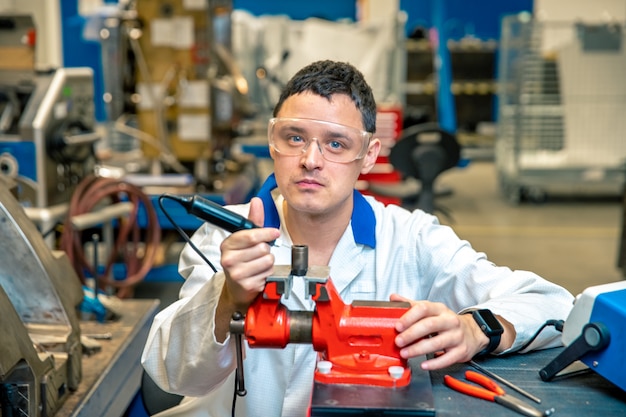 Worker in metal processing plant grinds metal component on vise