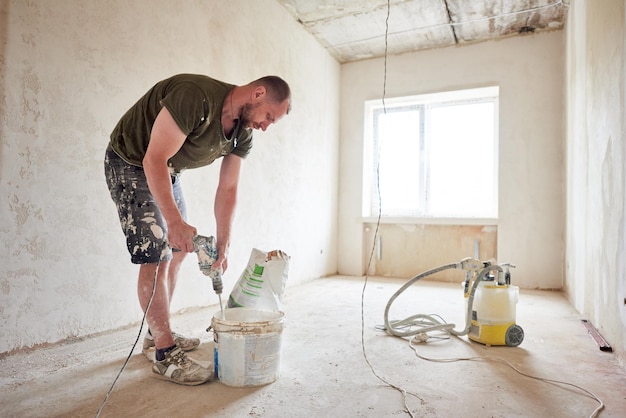 Worker mixing dry mortar with handheld mixer in bucket at repairable room