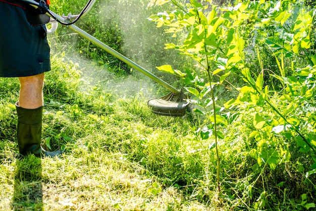 都市公園または裏庭で電気またはガソリンの芝刈り機を使用して背の高い草を刈る作業者ガーデニングケアツールおよび機器ハンドモアを使用した芝刈りのプロセス