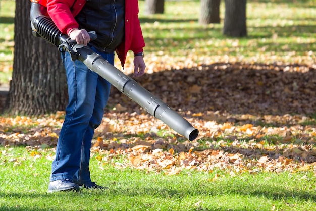 Foto operaio che opera un soffiatore per foglie per impieghi gravosi nel parco cittadino rimozione delle foglie cadute in autunno servizio di pulizia del parco