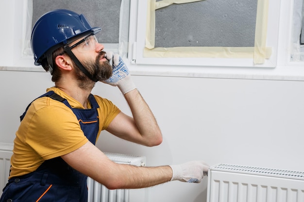 A worker in an orange helmet installs radiators in the house