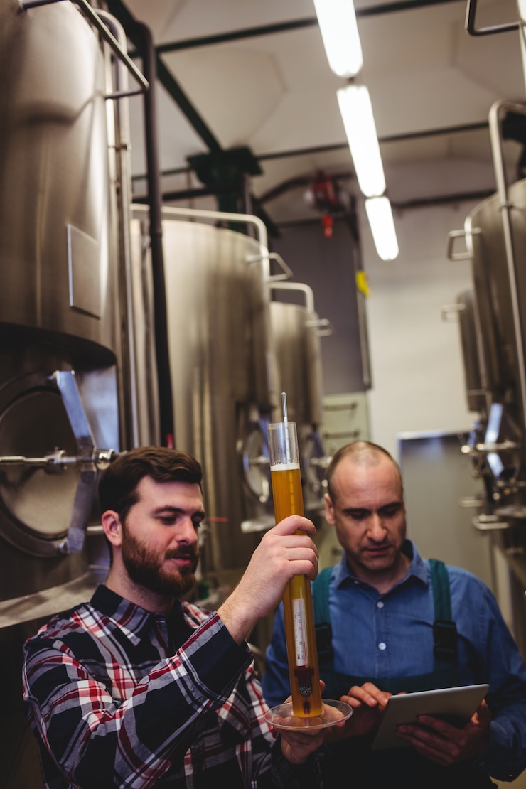 Photo worker and owner inspecting beer at brewery