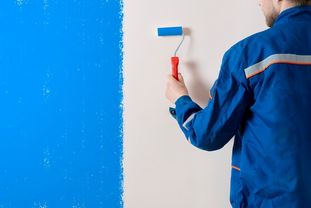 A worker painter painting the wall surface with a roller, man at work decorating a room