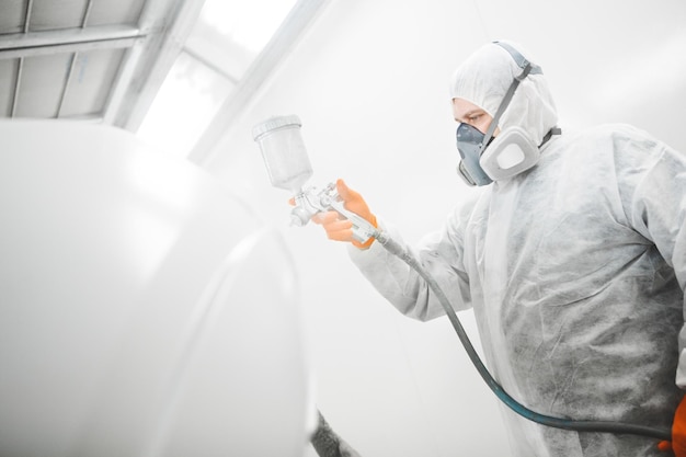 Worker paints auto with spray gun White car in a paint chamber during repair work