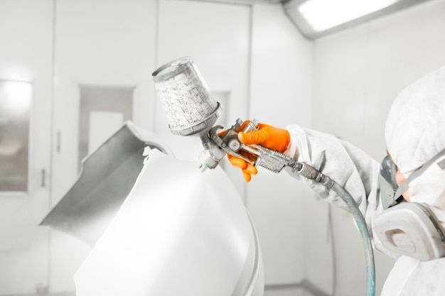 Worker paints auto with spray gun White car in a paint chamber during repair work