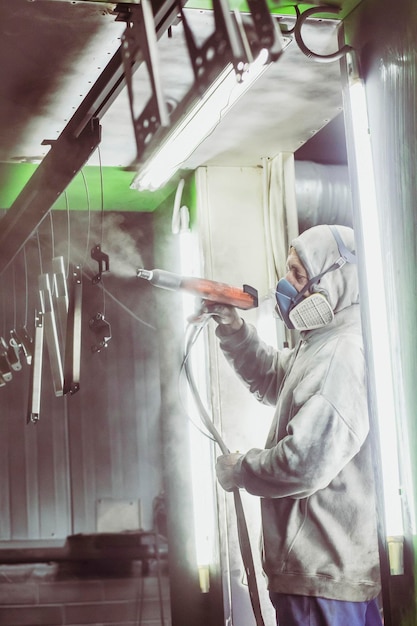 Worker paints metal parts in a factory