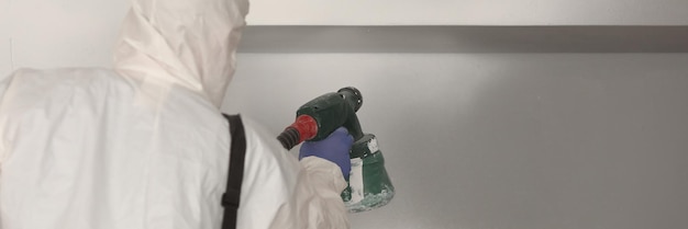 Worker paints wall white with spray gun