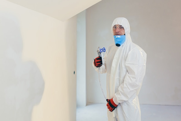 A worker paints the walls with a spray gun in a new building