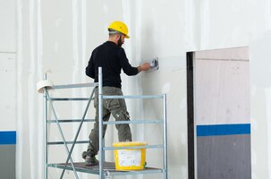 Worker plastering gypsum board wall.