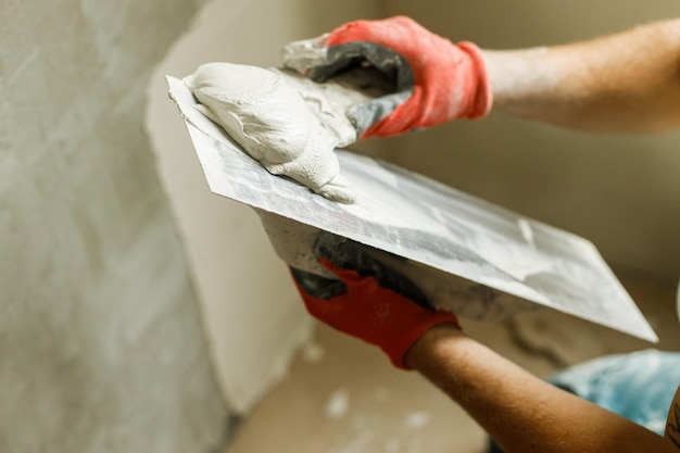 Foto operaio che intonaca le pareti con intonaco di gesso e spatola costruzione di casa e concetto di ristrutturazione domestica primo piano di mani in stucco e tuttofare con spatola