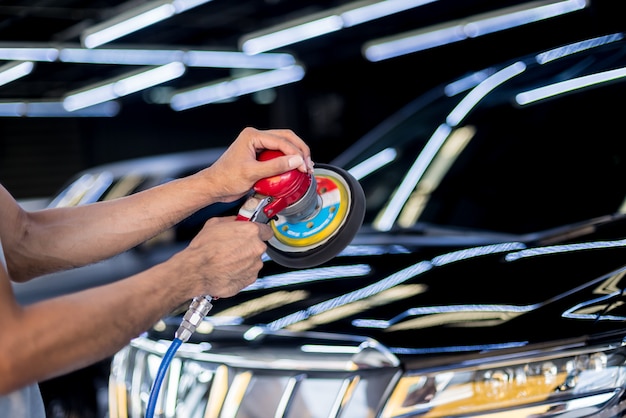 The worker polishes a car with the electric tool.