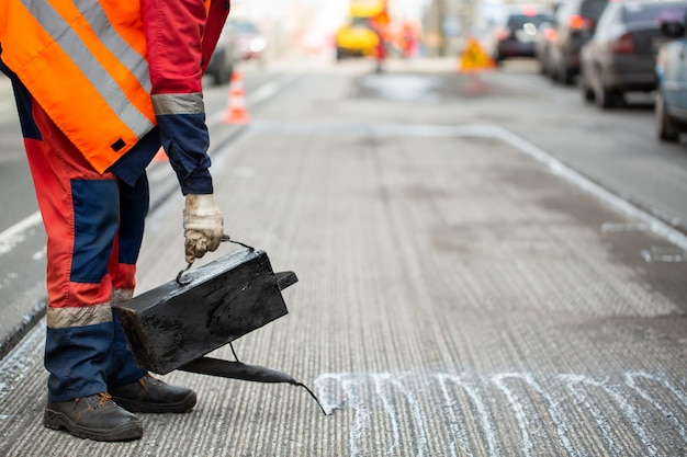 Un lavoratore versa bitume fuso asfalto liquido da un secchio di resina