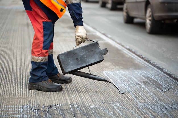 A worker pours liquid asphalt molten bitumen from a bucket of resin