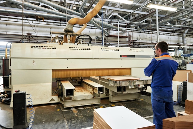 A worker processes furniture blanks on a machine tool in a\
factory. industrial production of furniture.