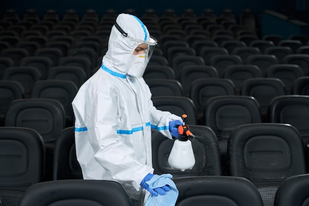 Worker in protective clothes cleaning cinema hall