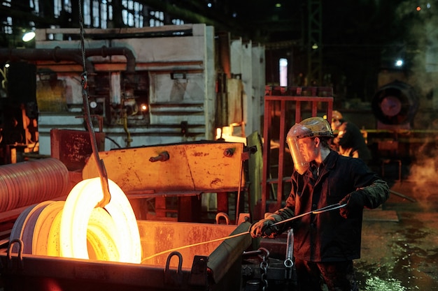 Photo worker in protective wear melting metal during his work in the factory