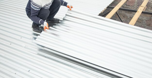 Worker puts the metal tiles on the roof of a house