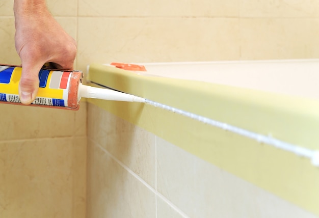 Worker puts silicone sealant to caulk the joint between tub and wall.