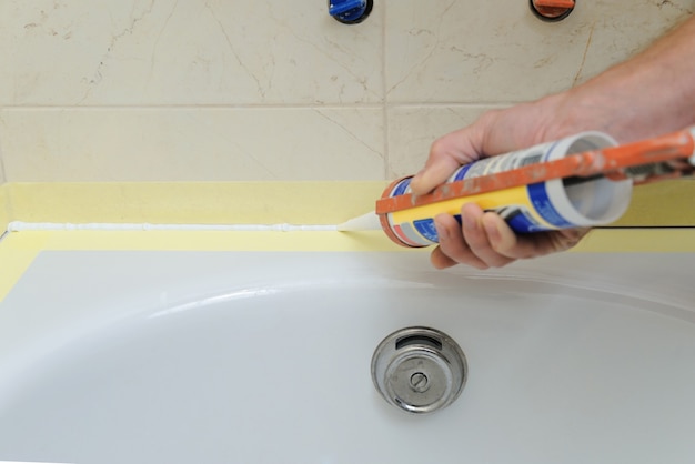 Worker puts silicone sealant to caulk the joint between tub and wall.