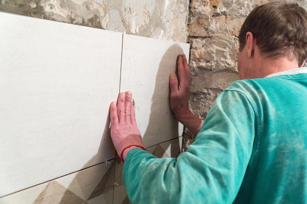 The worker puts tiles on the wall. Finishing works, blurred focus. The technology of laying tile.