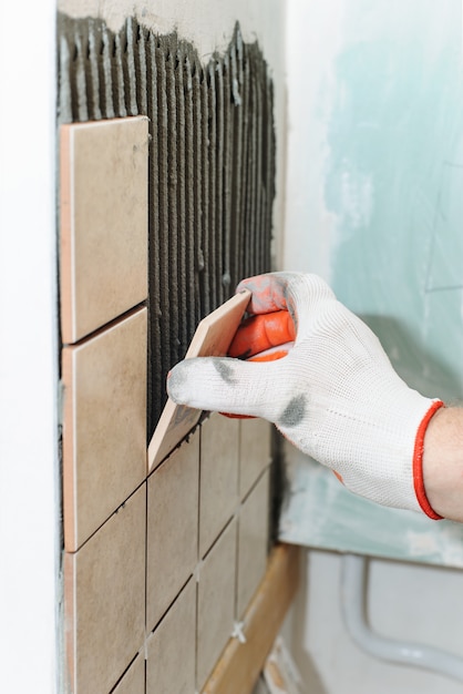 Lavoratore che mette le piastrelle sul muro in cucina.