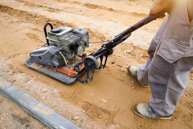 Foto il lavoratore sperona il terreno con una macchina vibrante