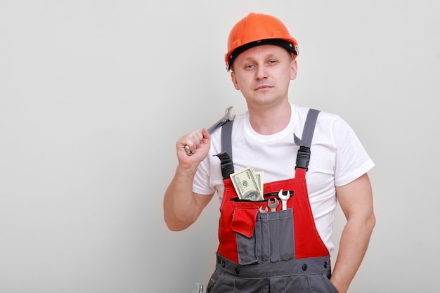 Worker in red uniform, protective hard hat holding bundle of dollars, cash money on white