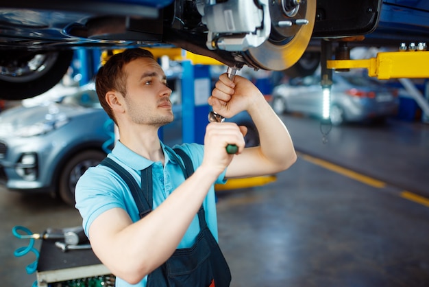 Worker repairing vehicle on lift, car service