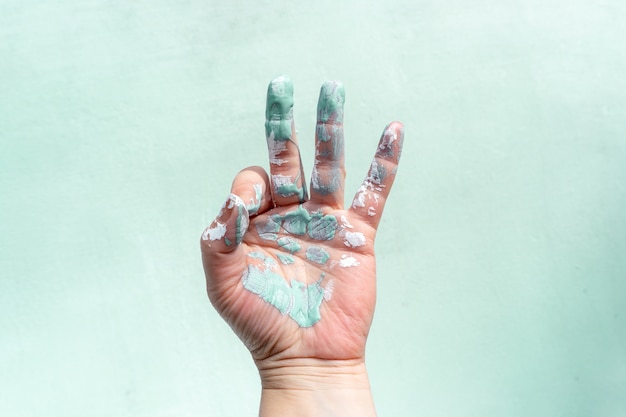 A worker's hand in paint shows an okay sign with his fingers while painting a wall.