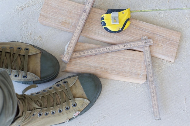 Foto scarpe da lavoro, strumento di misurazione, zoccolo in legno su un pavimento. sfondo