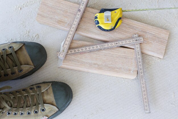 Foto scarpe da lavoro, strumento di misurazione, zoccolo in legno su un pavimento. sfondo