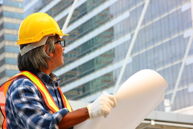 the worker in safety form holding plan and looking the construction site