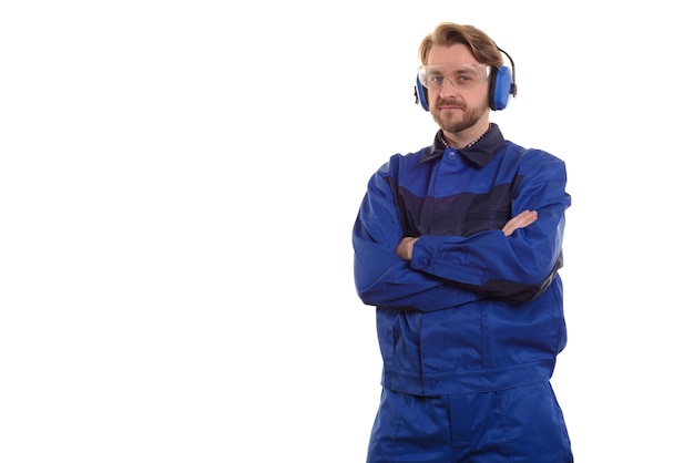 Worker in safety glasses and headphones stands with his arms crossed
