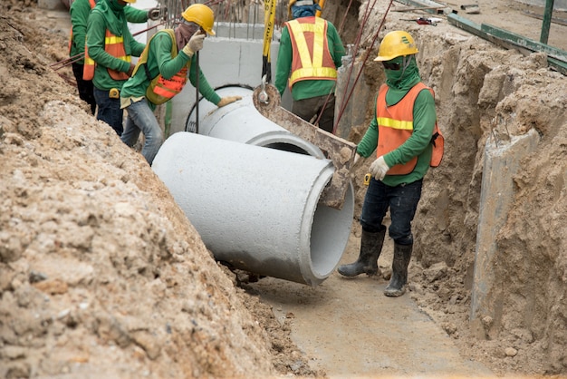 Il lavoratore in uniforme di sicurezza installa il drenaggio di tubi prefabbricati in calcestruzzo sotto terra