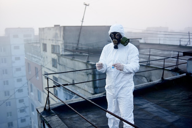 Worker scientist wearing protective coverall and gas mask doing ecological tests on the roof