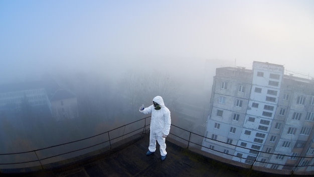 屋根の生態学的試験を行う保護カバーオールとガスマスクを身に着けている労働者の科学者
