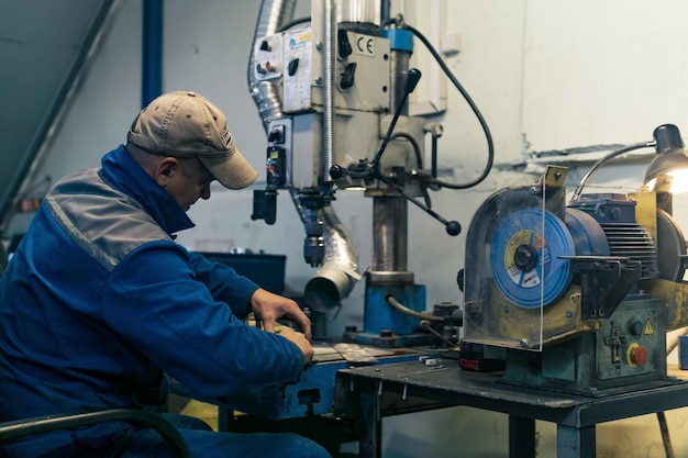 Il lavoratore in un'officina semibuia lavora su una perforatrice