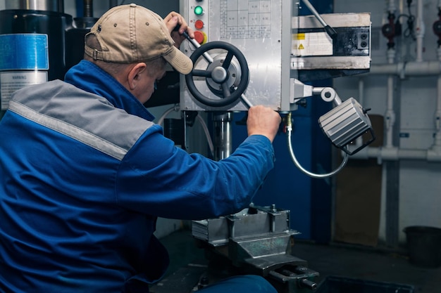 Worker in a semidark workshop works on a drilling machine