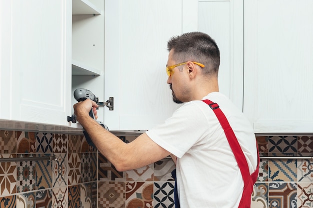 Photo the worker sets a new handle on the white cabinet with a screwdriver