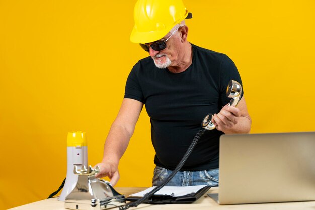 Worker in a spartan office is calling with a chrome phone isolated on yellow background