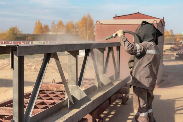 A worker in special clothing is sandblasting a metal building structure at an industrial site Industrial metal processing