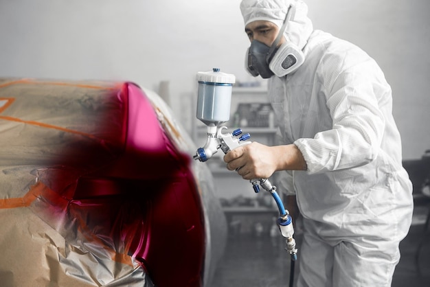 Foto lavoratore che spruzza vernice di colore raro e insolito con una pistola a spruzzo sul corpo dell'auto