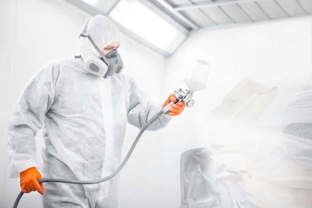 Worker spraying white paint with spray gun on car