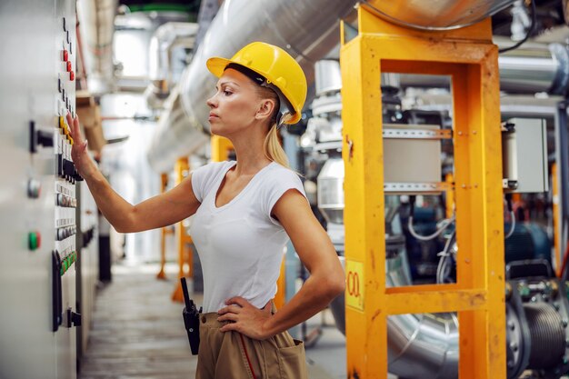 Worker standing next to dashboard in heating plant and adjusting settings